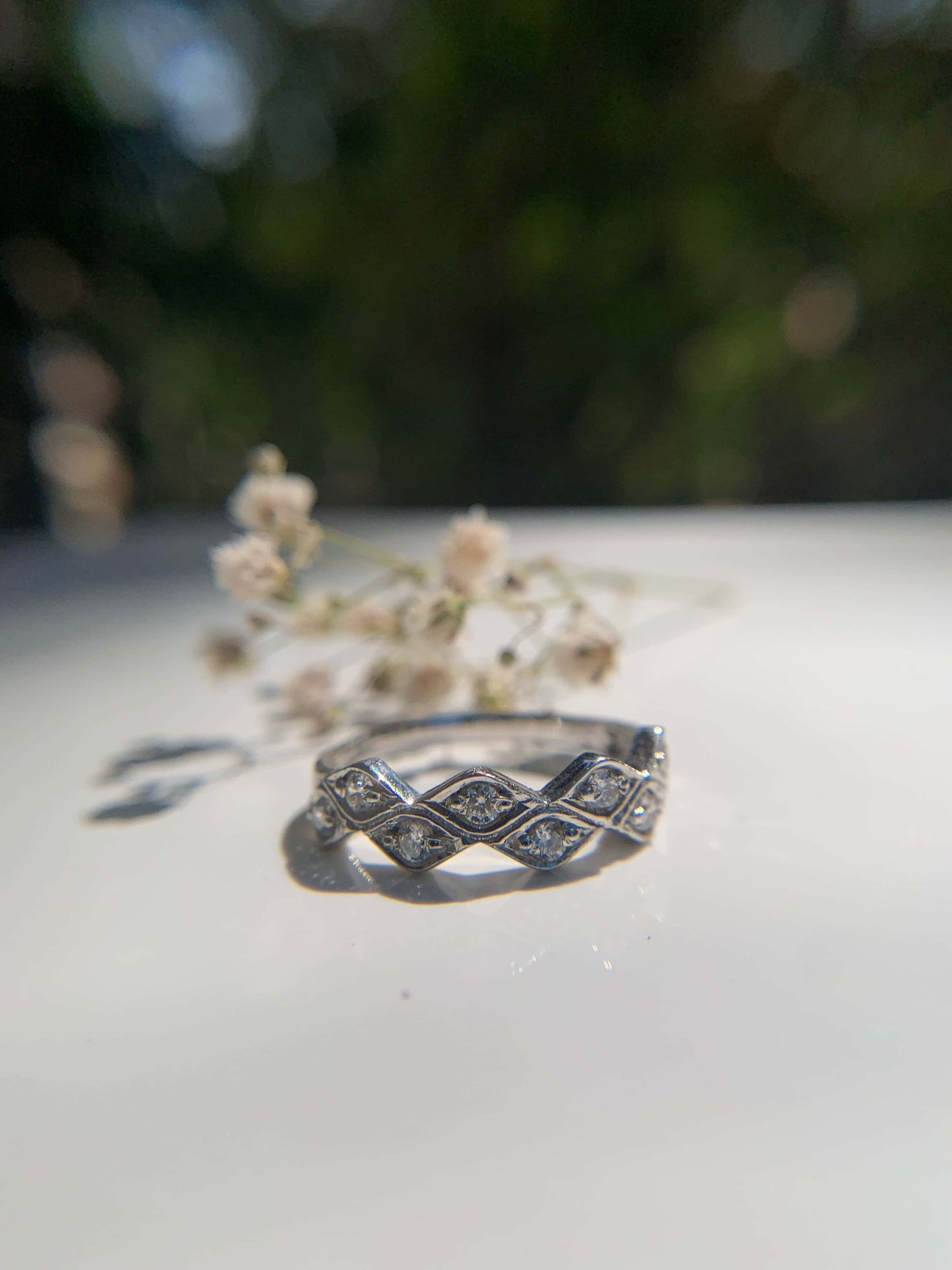 Marquese Ring with diamond details on a reflective surface, nature background.