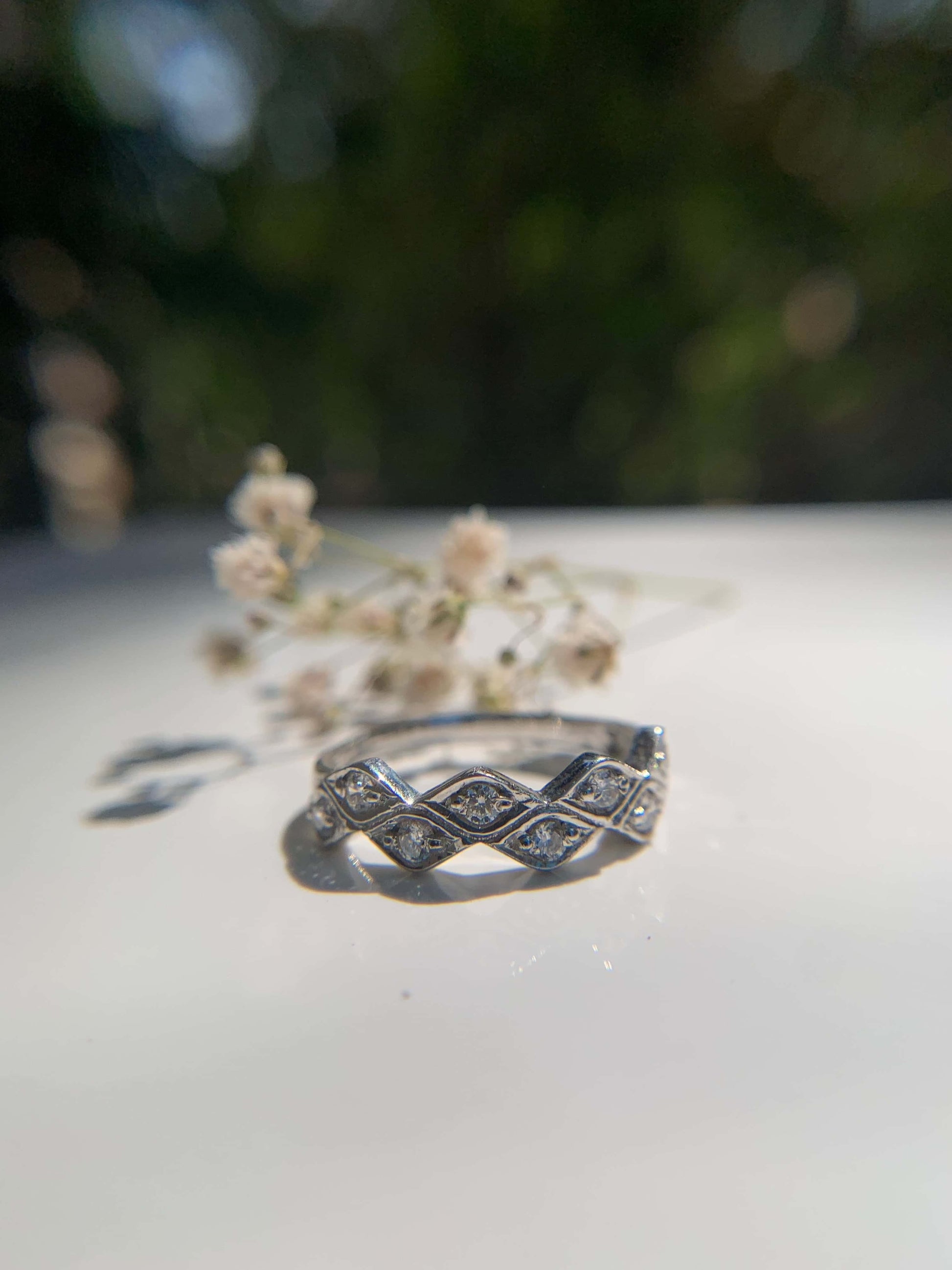 Marquese Ring with diamond details on a reflective surface, nature background.