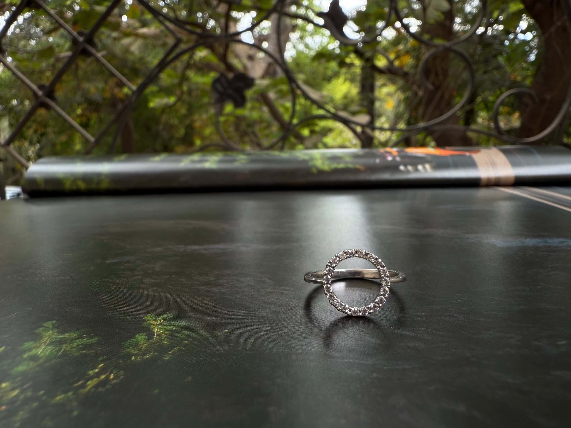 Halo ring with sparkling stones displayed outdoors on a reflective surface.