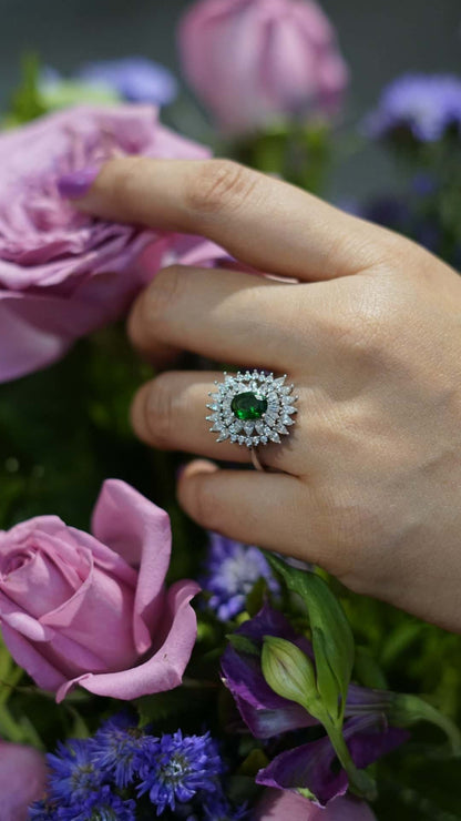 Hand wearing a green cocktail ring among purple flowers.