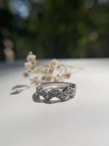 Marquese Ring with diamond details on a reflective surface, nature background.