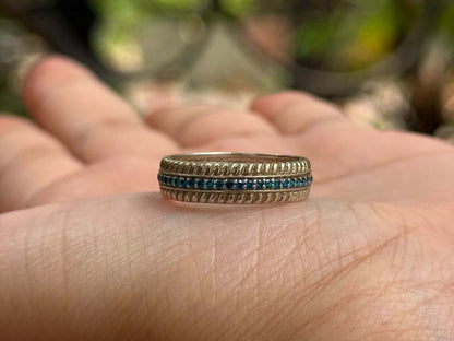 Gold ring with a central blue line detailing displayed on a hand.
