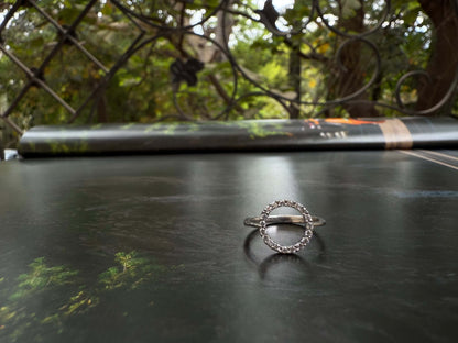 Halo ring with sparkling stones displayed outdoors on a reflective surface.